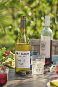 A bottle of Bonterra Pinot Gris open, on a table surrounded by glasses of water, wine, and cocktails with tapas.