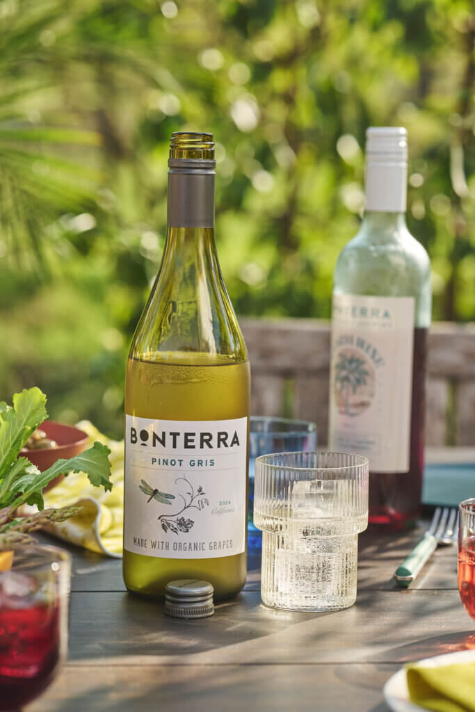 A bottle of Bonterra Pinot Gris open, on a table surrounded by glasses of water, wine, and cocktails with tapas.